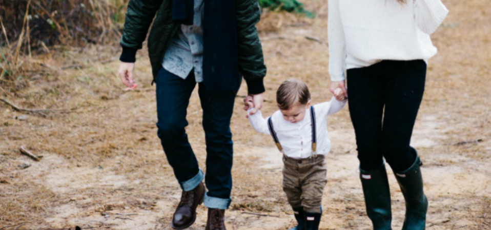 A child holding hands with his parents walking through mud